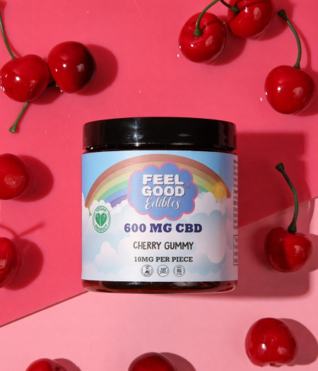 Cherry gummy CBD product jar surrounded by fresh cherries on a vibrant pink background.