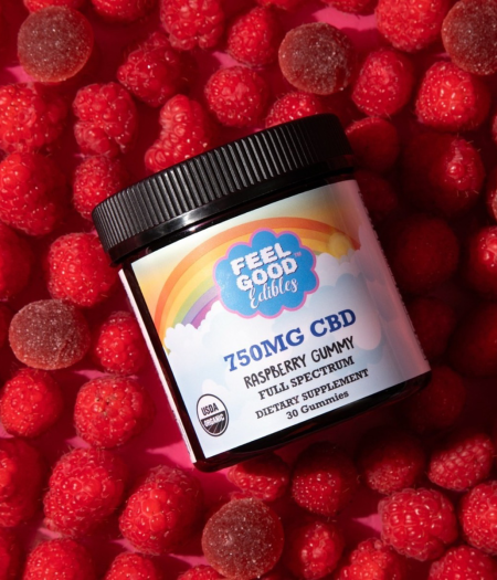 Raspberry gummies and fresh raspberries on a bright background with a jar labeled 750mg CBD dietary supplement.