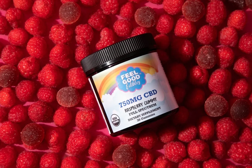 Premium raspberry gummy CBD candies surrounded by fresh raspberries, showcasing the product jar prominently.